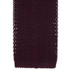 View 4 of product The Turnbull & Asser MTIE011-ZAI003 TIES 7.5CM is a plain burgundy tie shown rolled on a white background, featuring straight edges and textured knit—ideal for the modern gentleman’s versatile wardrobe.