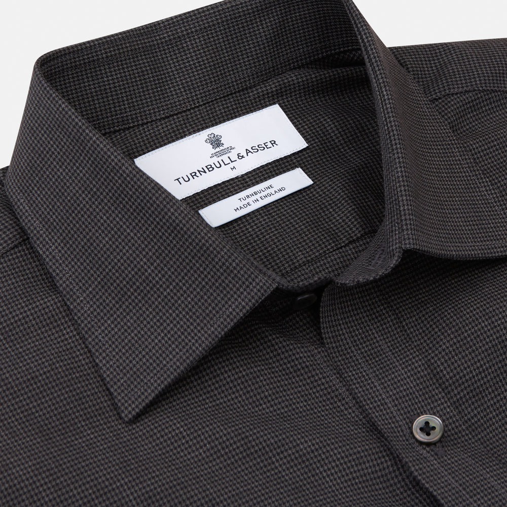 A man with short hair wears the Turnbull & Asser Black Check Weekend Fit Flannel Shirt with Derby Collar and 1-Button Cuffs, paired with light pants, against a plain background—ideal for a smart-casual weekend look.