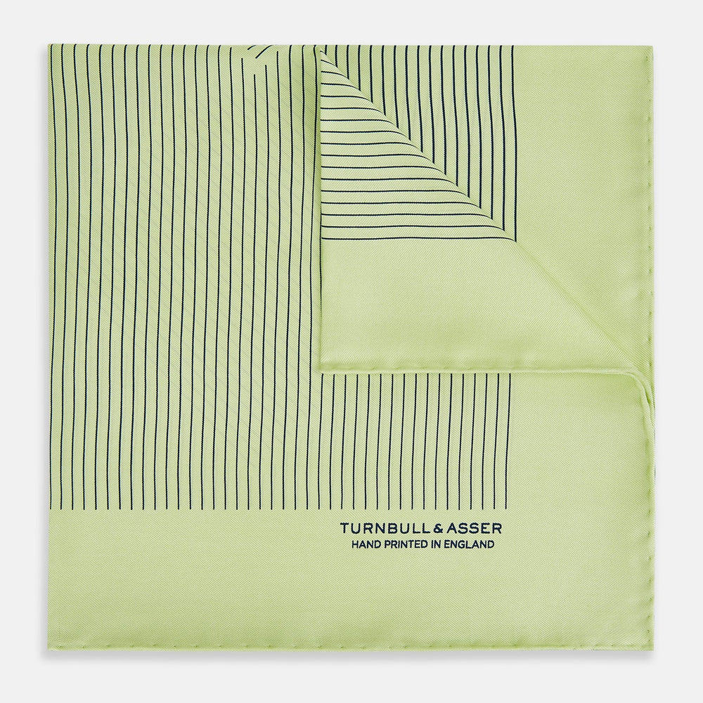 The Melon Green Stripe Silk Pocket Square by Turnbull & Asser features thin vertical black lines on light green silk, neatly folded to display both sides. The lower corner reads “TURNBULL & ASSER HAND PRINTED IN ENGLAND.”.