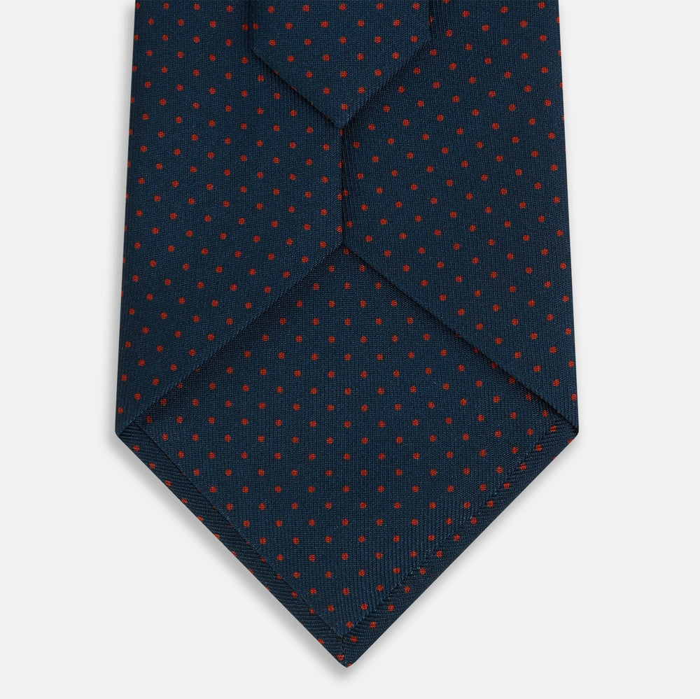 The Turnbull & Asser Navy and Red Polka Dot Silk Tie, rolled neatly on a light background, highlights classic British craftsmanship with its refined pattern.