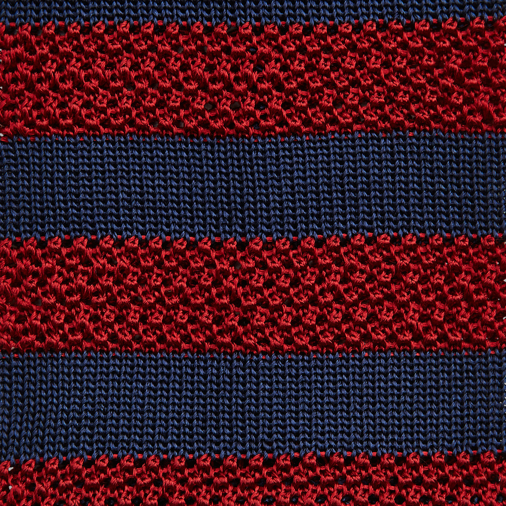 The Turnbull & Asser KNITTED STRIPE RED TIE features bold red and navy wide stripes in a rolled-up, knitted design—an eye-catching accessory shown on a plain white background.