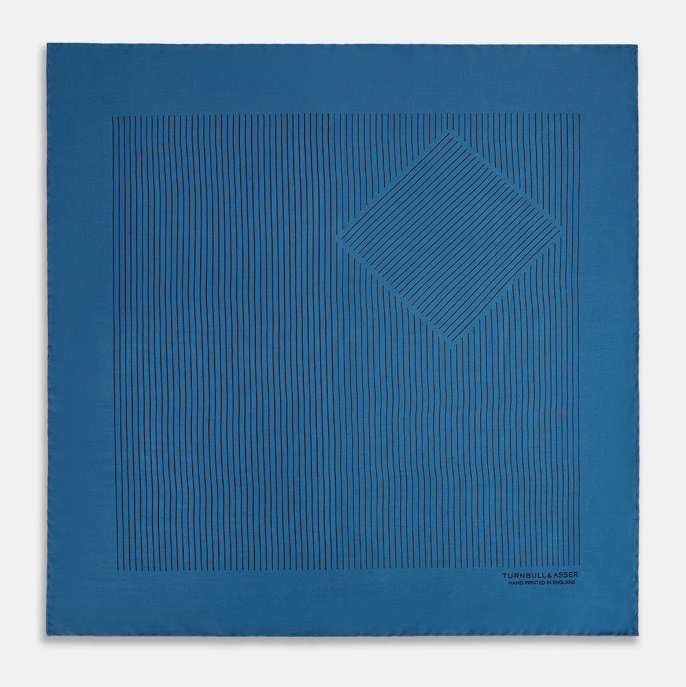 The Blue Stripe Silk Pocket Square by Turnbull & Asser features thin vertical lines, British heritage details, and "TURNBULL & ASSER HAND PRINTED IN ENGLAND" printed on the fabric, with one corner folded to reveal the reverse side.