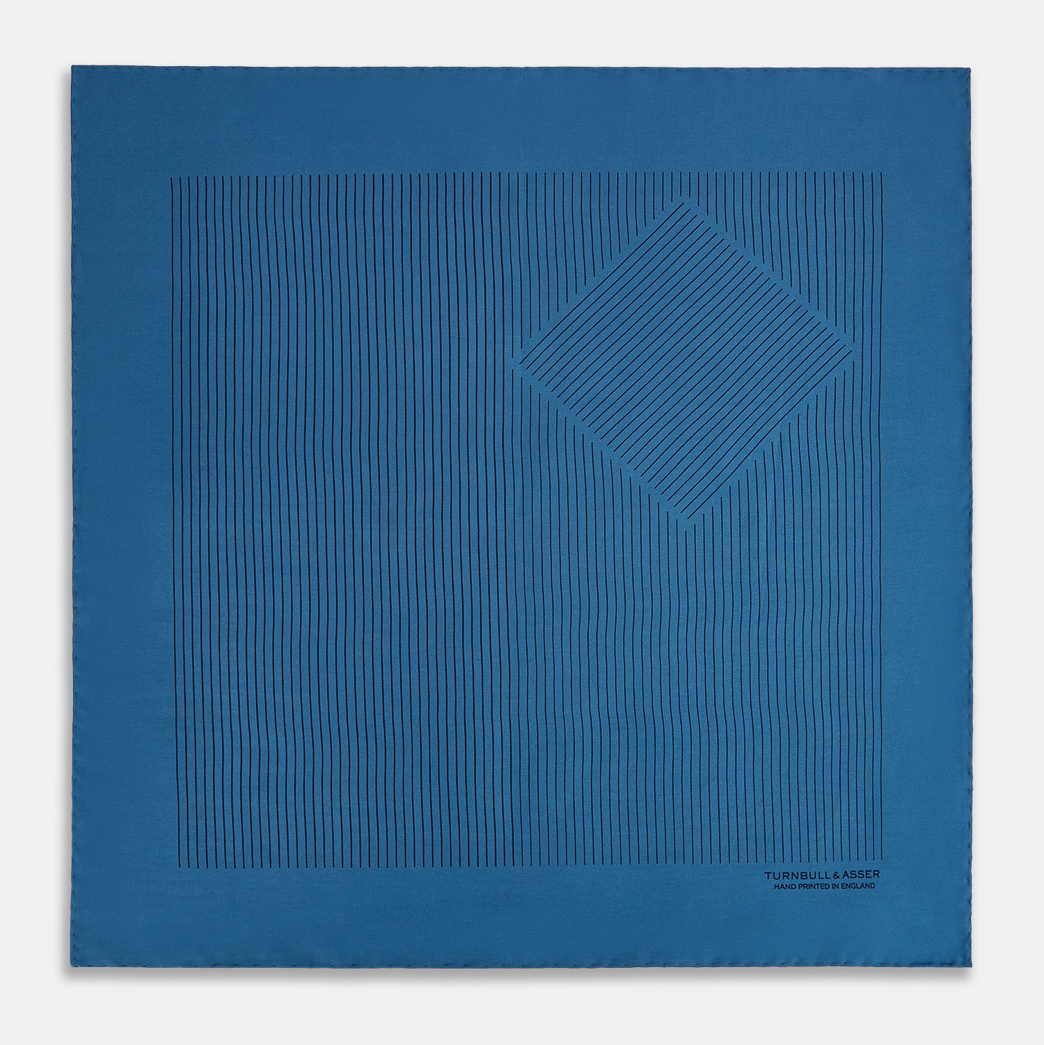 View 3 of product The Blue Stripe Silk Pocket Square by Turnbull & Asser features thin vertical lines, British heritage details, and "TURNBULL & ASSER HAND PRINTED IN ENGLAND" printed on the fabric, with one corner folded to reveal the reverse side.