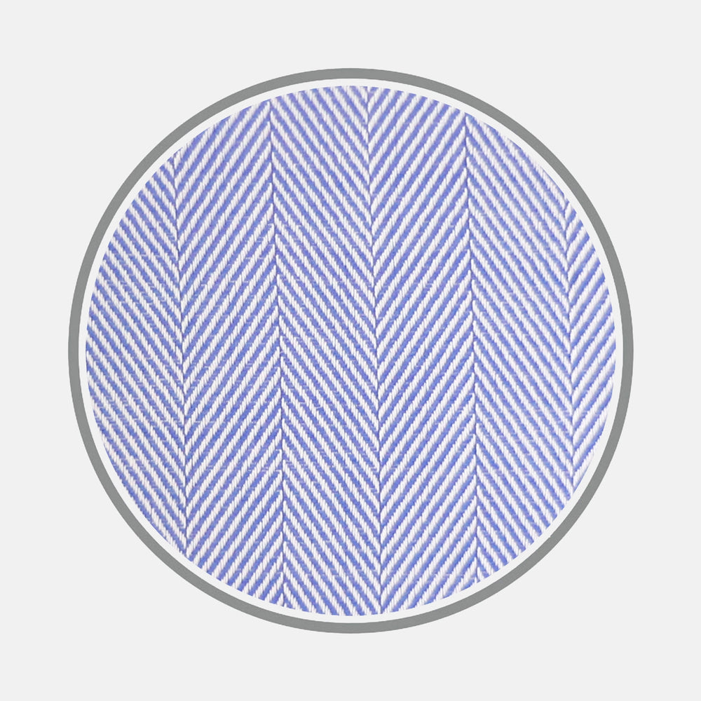 Close-up of a circular swatch of Turnbull & Asser’s Blue Herringbone Cotton Fabric, featuring a light blue diagonal zigzag pattern bordered in gray on a white background.