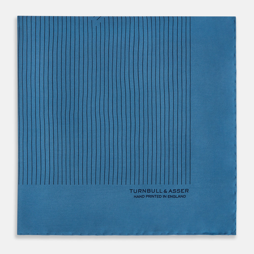 The Blue Stripe Silk Pocket Square by Turnbull & Asser features thin vertical lines, British heritage details, and "TURNBULL & ASSER HAND PRINTED IN ENGLAND" printed on the fabric, with one corner folded to reveal the reverse side.