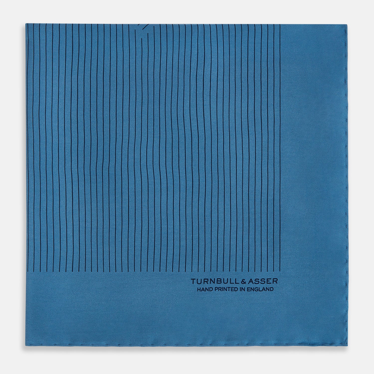 View 4 of product The Blue Stripe Silk Pocket Square by Turnbull & Asser features thin vertical lines, British heritage details, and "TURNBULL & ASSER HAND PRINTED IN ENGLAND" printed on the fabric, with one corner folded to reveal the reverse side.