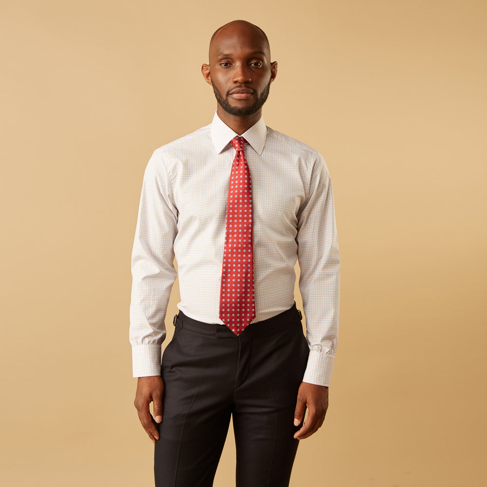 A man stands against a beige background, facing forward with a neutral expression and arms relaxed, wearing the Turnbull & Asser Red Multi Check Regular Fit Mayfair Shirt.