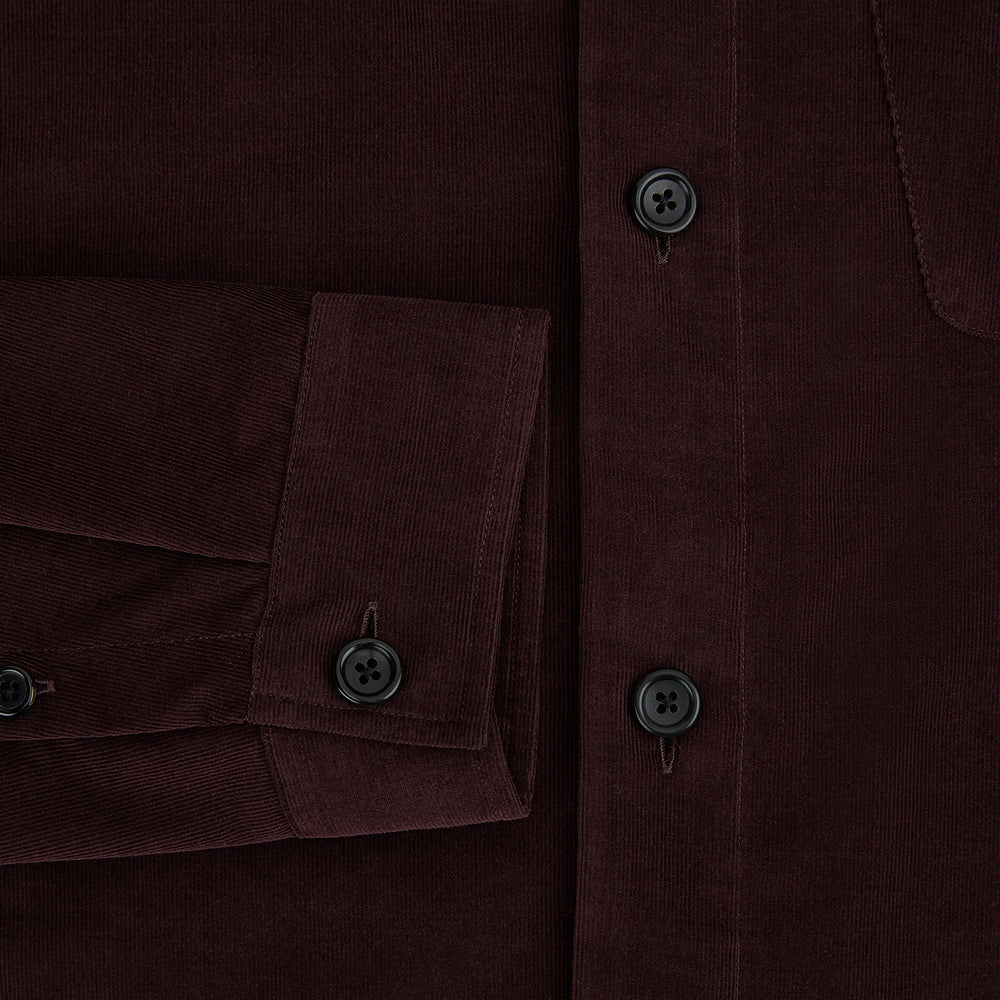 The Turnbull & Asser Burgundy Corduroy Hampstead Overshirt features long sleeves, a collar, a large left chest pocket, and two zippered side pockets, shown laid flat on a plain white background.