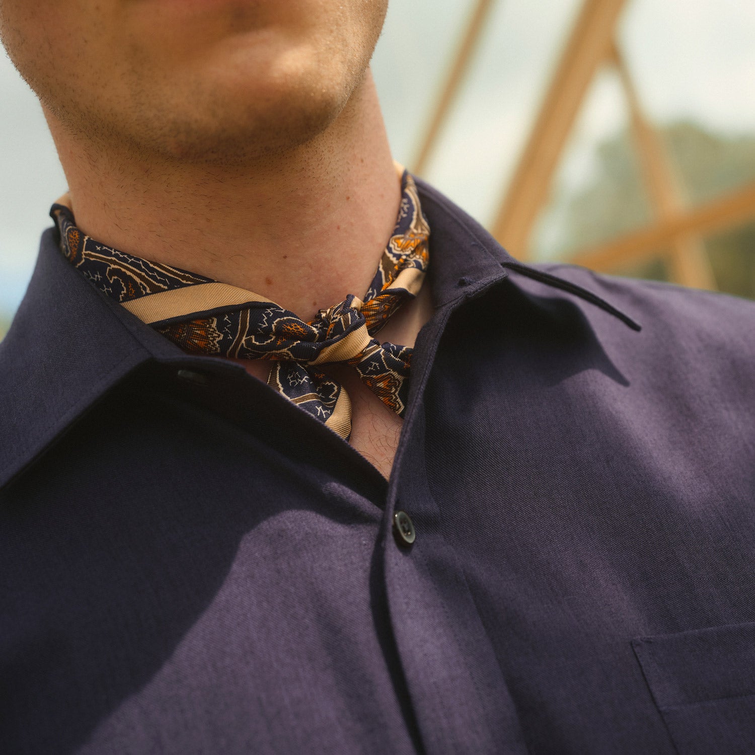 View 4 of product A man stands against a beige background wearing the Turnbull & Asser Navy Weekend Fit Cotton & Wool Shirt with a Derby collar and 1 button cuffs, paired with brown pants and black shoes, looking to the side with a neutral expression.