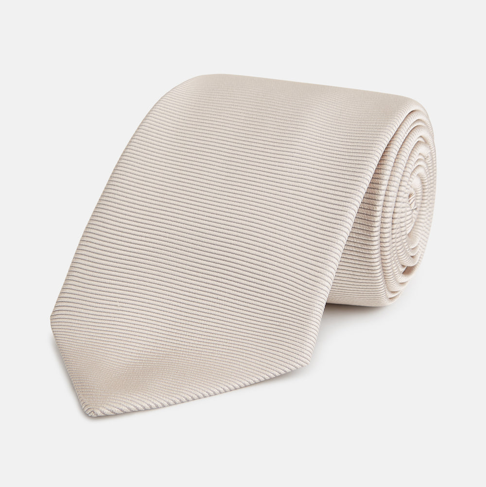 The Turnbull & Asser HORIZONTAL TWILL VELLUM TIE, a light beige silk necktie with a subtle ribbed texture, is shown rolled up on a white background—an essential finishing touch for smart attire.