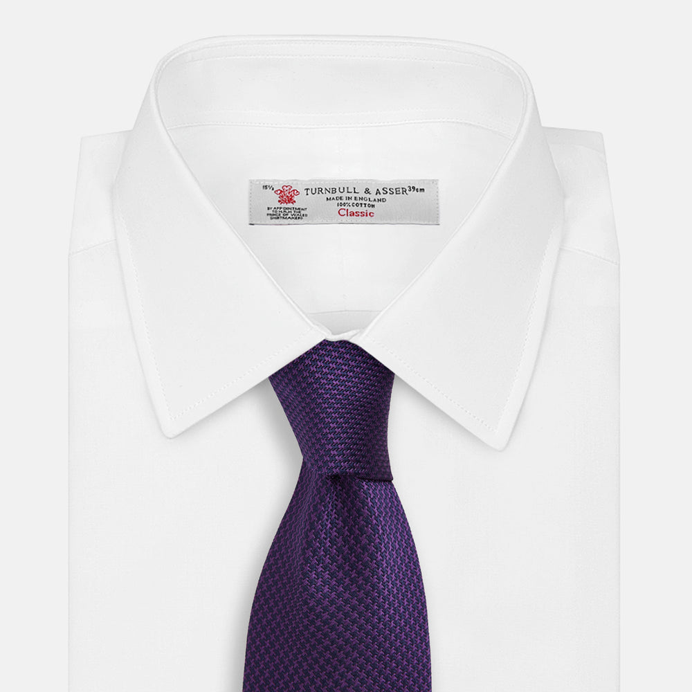 The HOUNDSTOOTH NAVY PLUM TIE by Turnbull & Asser, featuring a textured pattern, is showcased rolled up against a plain white background—an essential accessory.