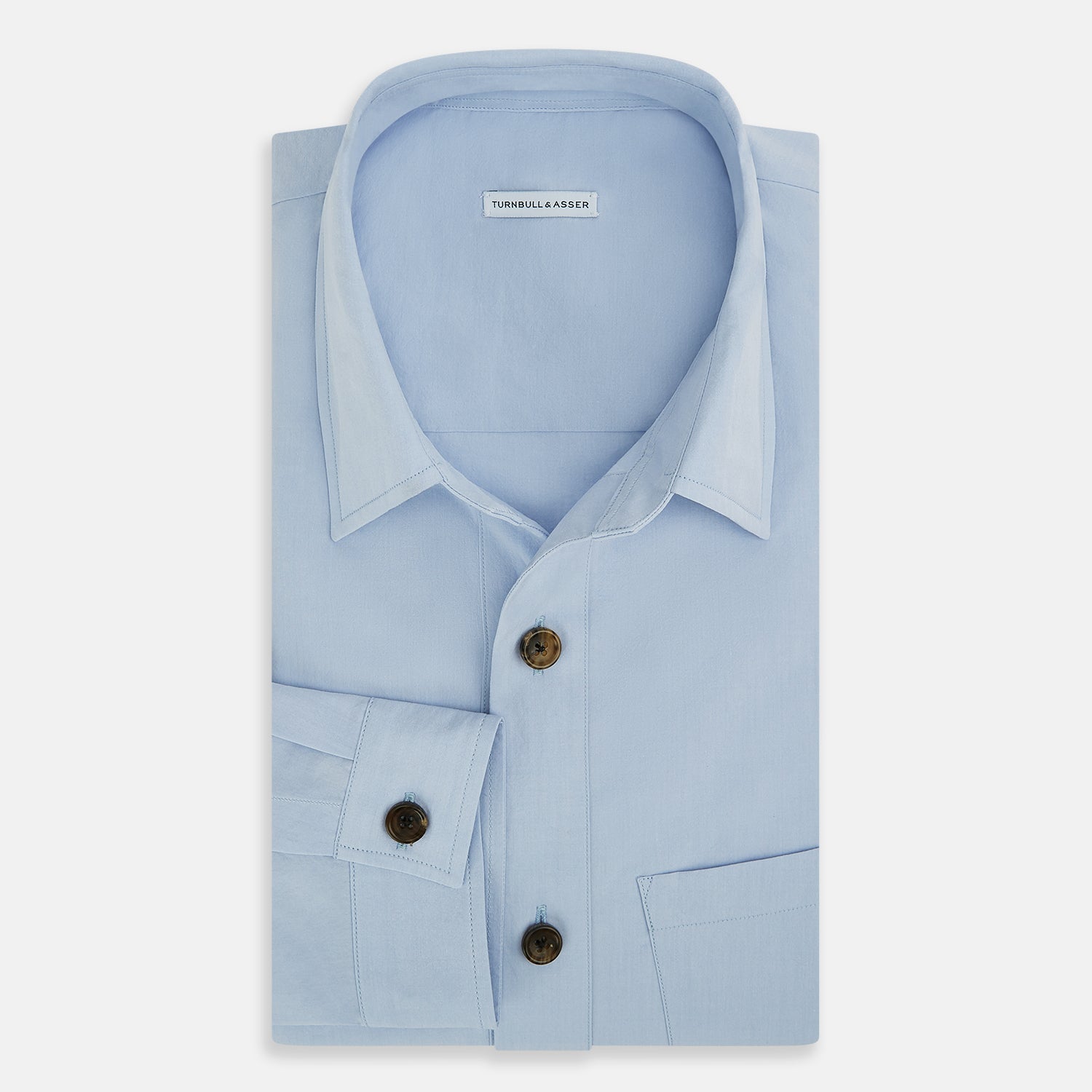 View 5 of product The Turnbull & Asser Pale Blue Hyde Overshirt is a long-sleeve, sanforised cotton button-up with a single chest pocket and dark buttons, shown on a plain white background.
