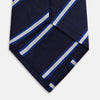 View 4 of product The White and Navy Blazer Silk Tie by Turnbull & Asser features diagonal white and light blue stripes on navy silk, shown rolled on a white background. A refined choice to complement any office shirt.