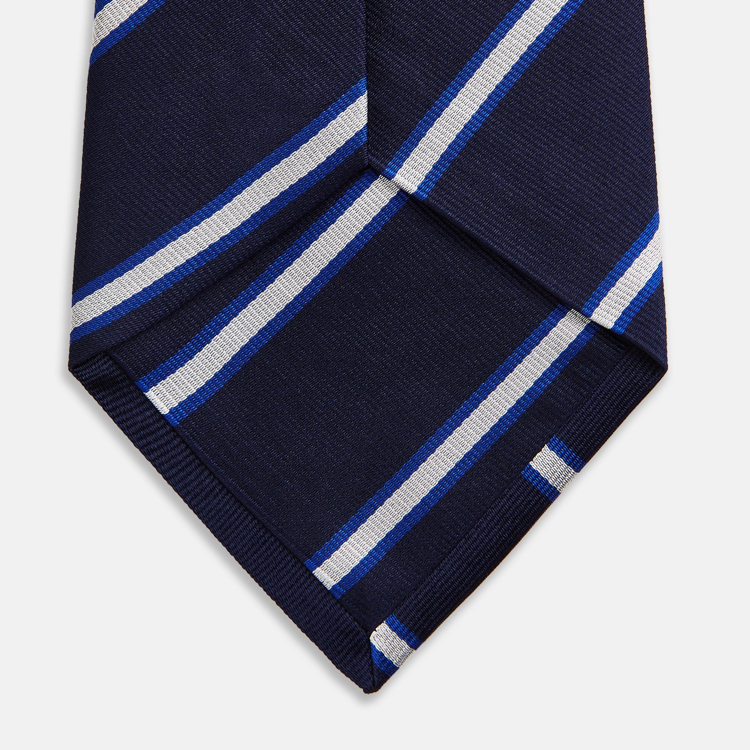 View 4 of product The White and Navy Blazer Silk Tie by Turnbull & Asser features diagonal white and light blue stripes on navy silk, shown rolled on a white background. A refined choice to complement any office shirt.
