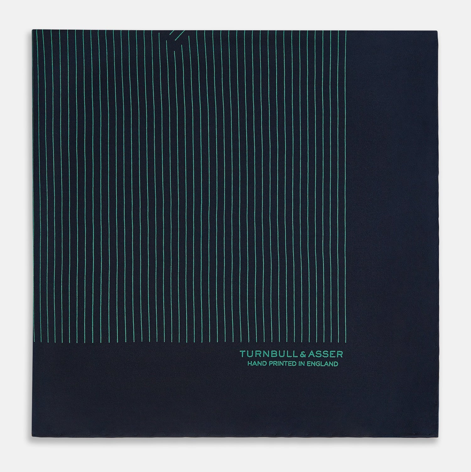 View 4 of product A Navy and Petrol Green Stripe Silk Pocket Square by Turnbull & Asser, featuring thin petrol green stripes and "Turnbull & Asser Hand Printed in England" in the bottom right corner. One corner is folded to display hand-rolled edges.
