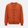View 1 of product The Orange Cashmere Cardigan by Turnbull & Asser showcases vibrant burnt orange, a V-neck, dark buttons, ribbed cuffs and hem, long sleeves, and two front pockets. Part of the knitwear collection; displayed on a white background.