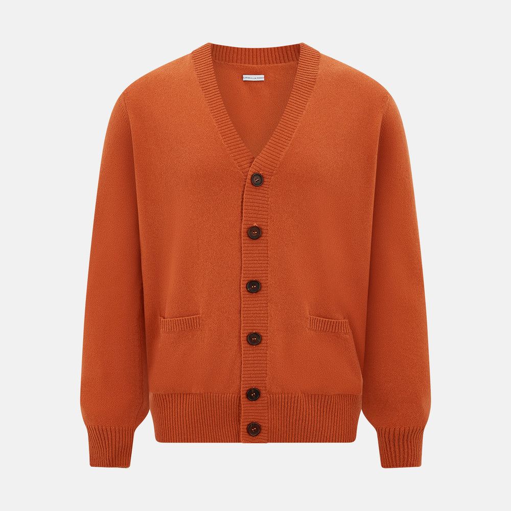 The Orange Cashmere Cardigan by Turnbull & Asser showcases vibrant burnt orange, a V-neck, dark buttons, ribbed cuffs and hem, long sleeves, and two front pockets. Part of the knitwear collection; displayed on a white background.