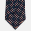 View 3 of product The Turnbull & Asser Navy and Red Circle Foulard Silk Tie, featuring a repeating red and white circular motif, is neatly rolled to display classic British craftsmanship.