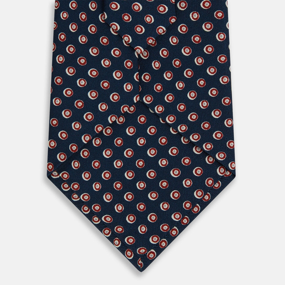 The Turnbull & Asser Navy and Red Circle Foulard Silk Tie, featuring a repeating red and white circular motif, is neatly rolled to display classic British craftsmanship.