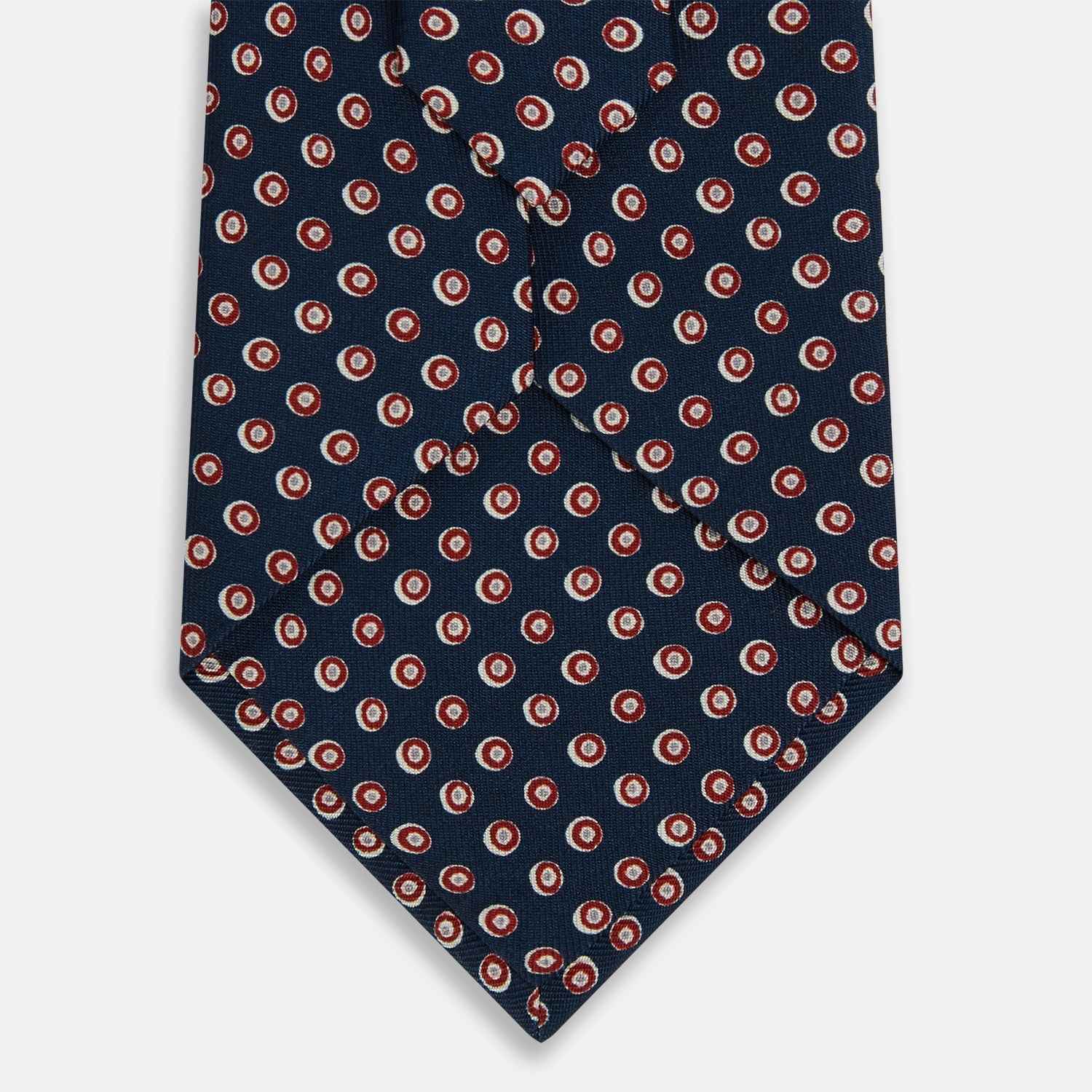 View 3 of product The Turnbull & Asser Navy and Red Circle Foulard Silk Tie, featuring a repeating red and white circular motif, is neatly rolled to display classic British craftsmanship.