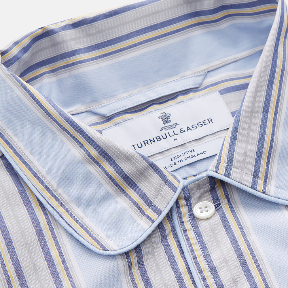 The Pale Blue and Yellow Multi Stripe Cotton Sussex Nightshirt by Turnbull & Asser features long sleeves, a knee-length cut, a collar, button-down front, chest pocket, and rounded hem.