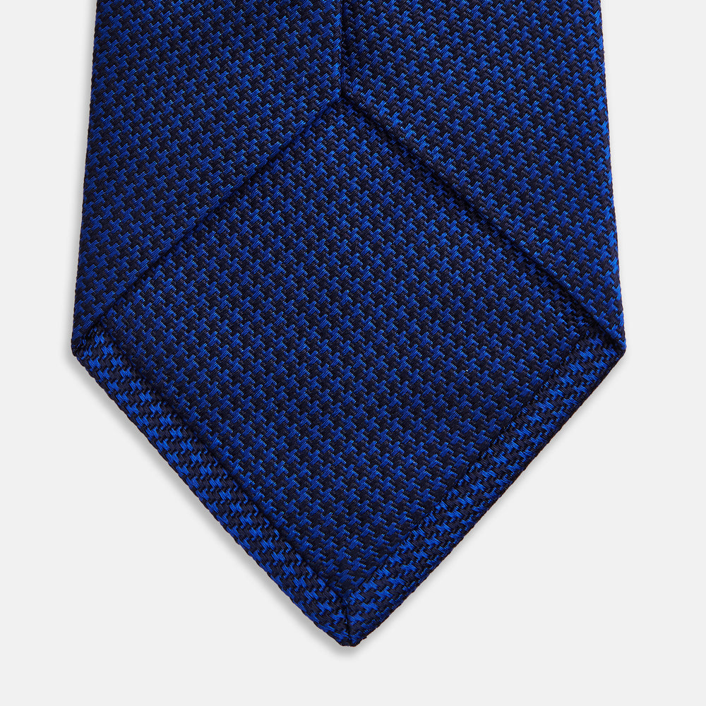 The HOUNDSTOOTH NAVY CRUISE TIE by Turnbull & Asser, featuring a textured blue design, is displayed rolled-up on a plain white background—an essential accessory for elevating formal looks.