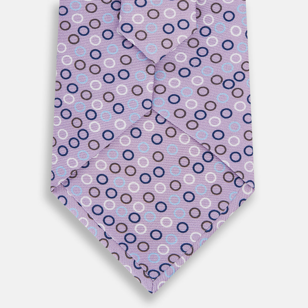 The Turnbull & Asser Multi-coloured Circle Lilac Silk Tie features overlapping blue, purple, and white circles on fine English silk—ideal for elevating smart outfits. Shown rolled against a plain white background.