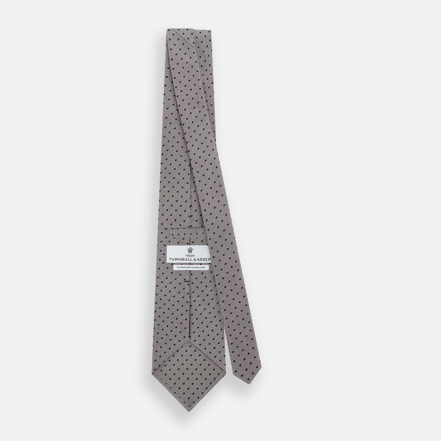 View 4 of product The Turnbull & Asser Navy and Lilac Micro Dot Silk Tie is shown rolled up on a white background, featuring a refined pattern of small lilac dots on navy silk.