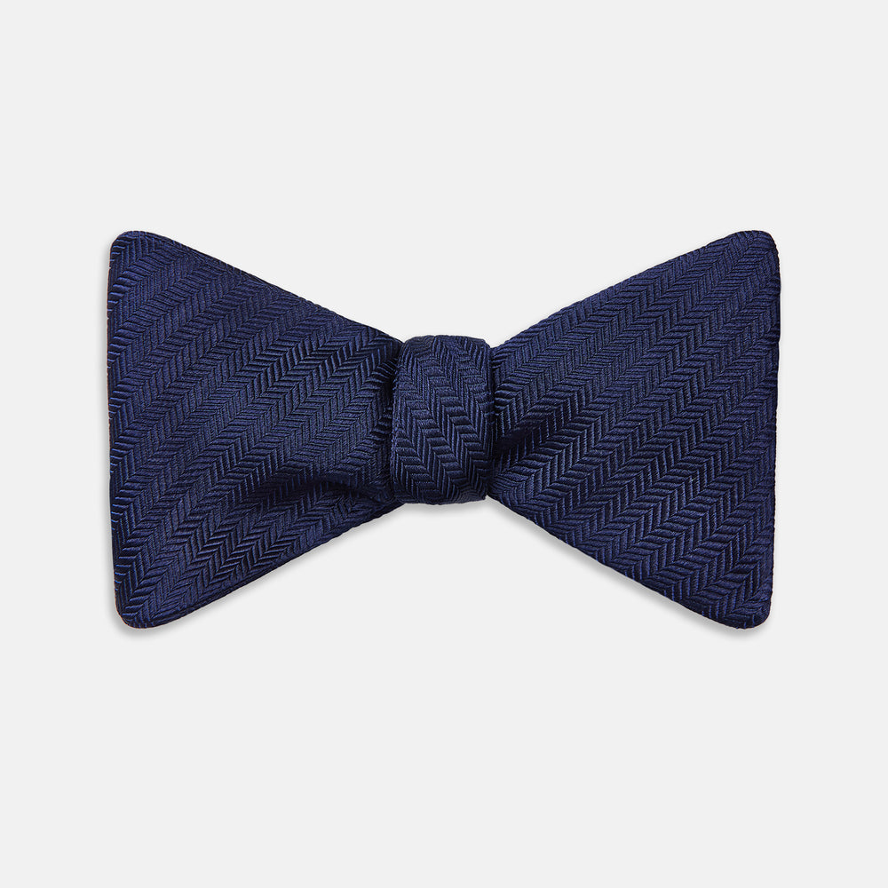 The Turnbull & Asser HERRINGBONE NAVY BOW TIE features a subtle herringbone pattern in navy blue, shown against a plain white background—the perfect accessory to elevate any smart look.