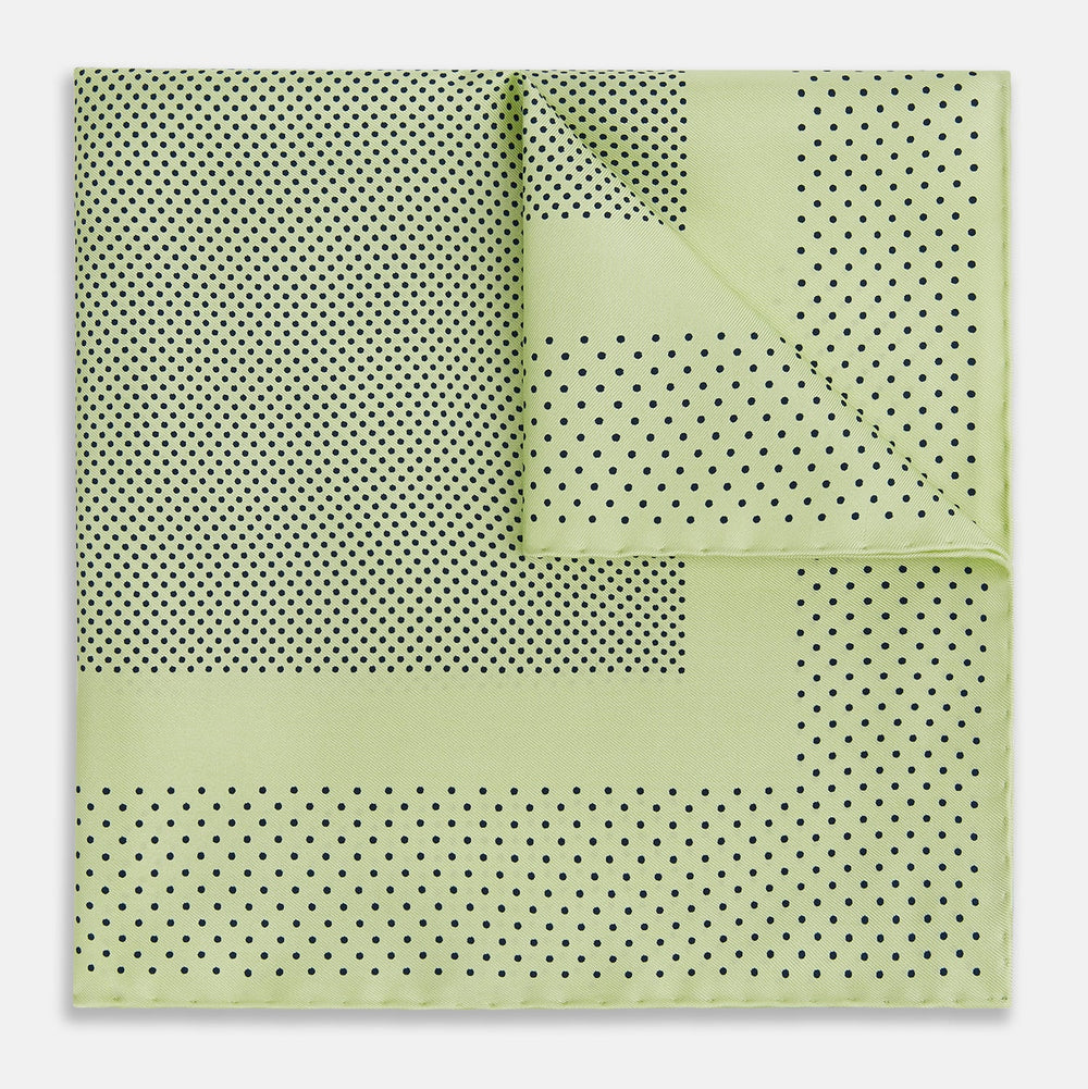 The Melon Green Dot Silk Pocket Square by Turnbull & Asser is handmade in England from silk, featuring small black polka dots. Shown folded with a turned-up corner, it displays both sides of the light green fabric.