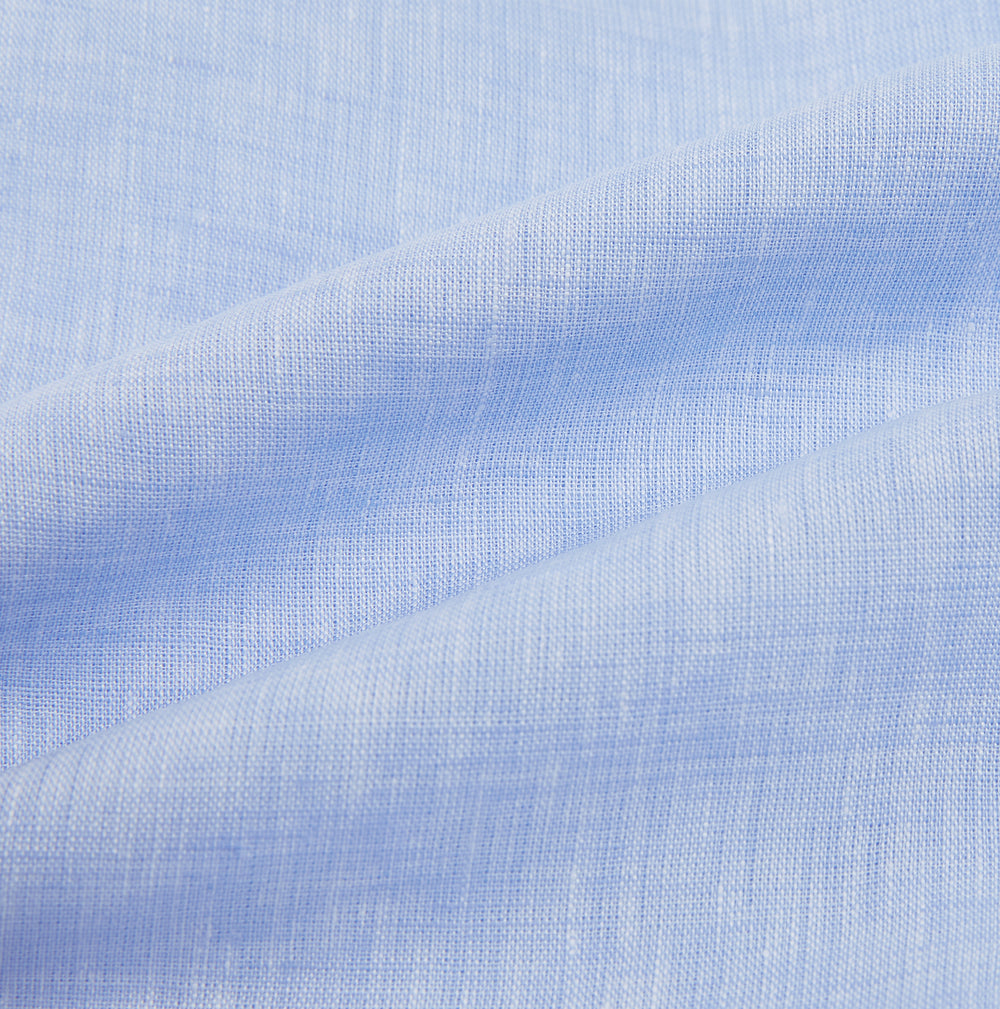 The Turnbull & Asser Pale Blue Linen Mayfair Shirt features a collar, front pocket, and white buttons. This long-sleeve shirt is displayed on a white background.