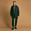 View 1 of product A man stands against a beige background, wearing the Turnbull & Asser Navy Burrows Double Breasted Coat over a plaid shirt and mauve cardigan, paired with dark rolled-up jeans and black shoes, looking directly at the camera with a neutral expression.