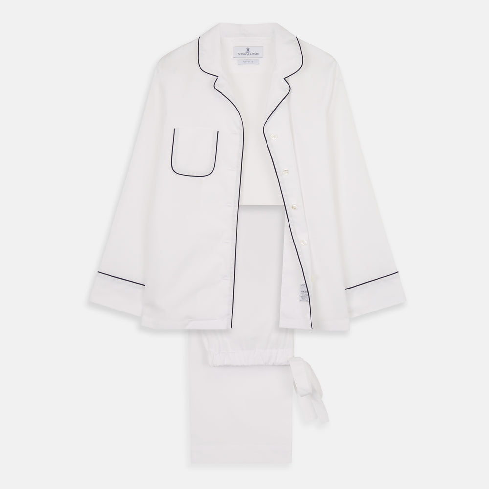 The Turnbull & Asser Women's Harriet Plain White Cotton Pyjama Set features long sleeves, black piping, a chest pocket, and matching pants with elastic waistband and ribbon tie, all displayed on a white background.