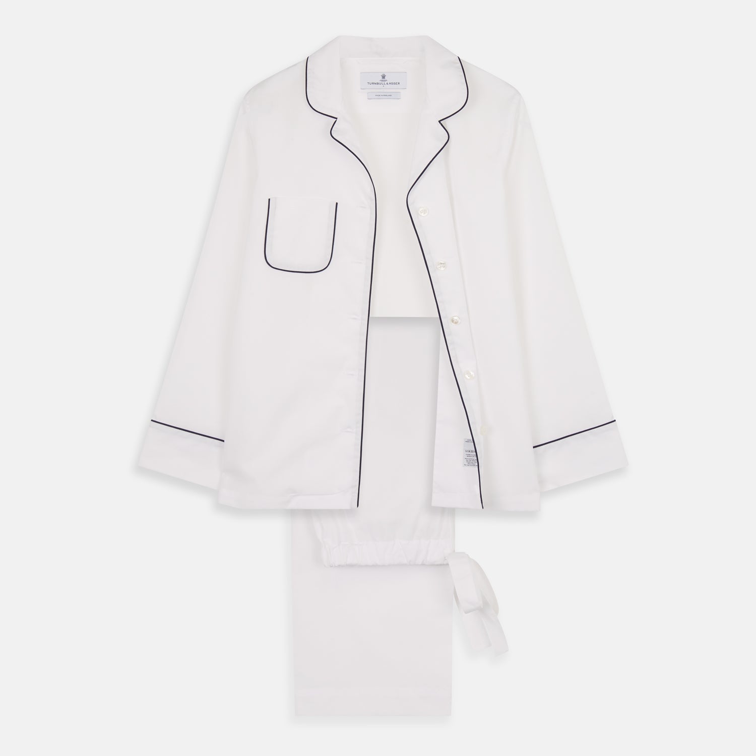 View 1 of product The Turnbull & Asser Women's Harriet Plain White Cotton Pyjama Set features long sleeves, black piping, a chest pocket, and matching pants with elastic waistband and ribbon tie, all displayed on a white background.