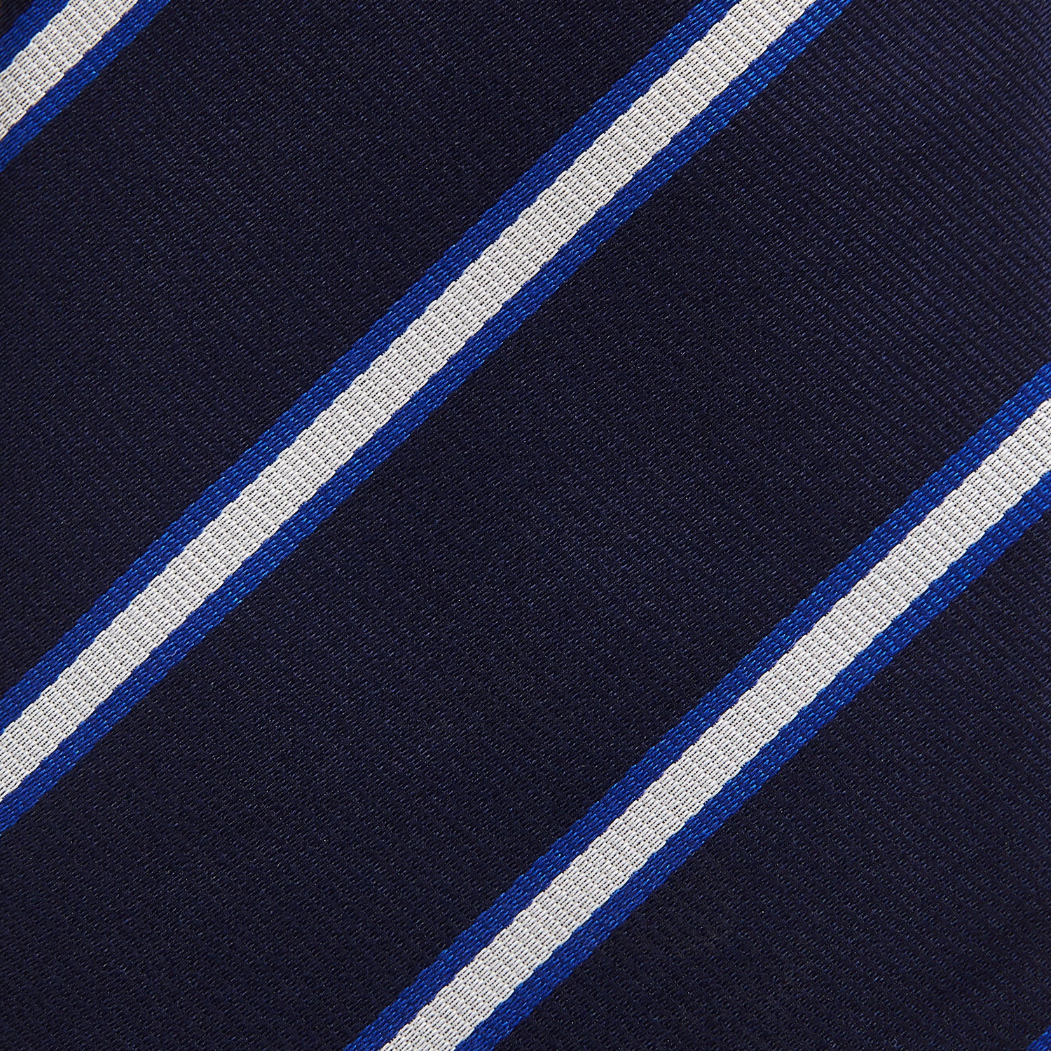View 3 of product The White and Navy Blazer Silk Tie by Turnbull & Asser features diagonal white and light blue stripes on navy silk, shown rolled on a white background. A refined choice to complement any office shirt.