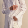 View 6 of product A person with curly hair wears the Turnbull and The Deck White Cotton Minimalist Shirt by Turnbull & Asser, paired with pants. Posed against a plain background, their minimalist silhouette is highlighted in this black and white image.