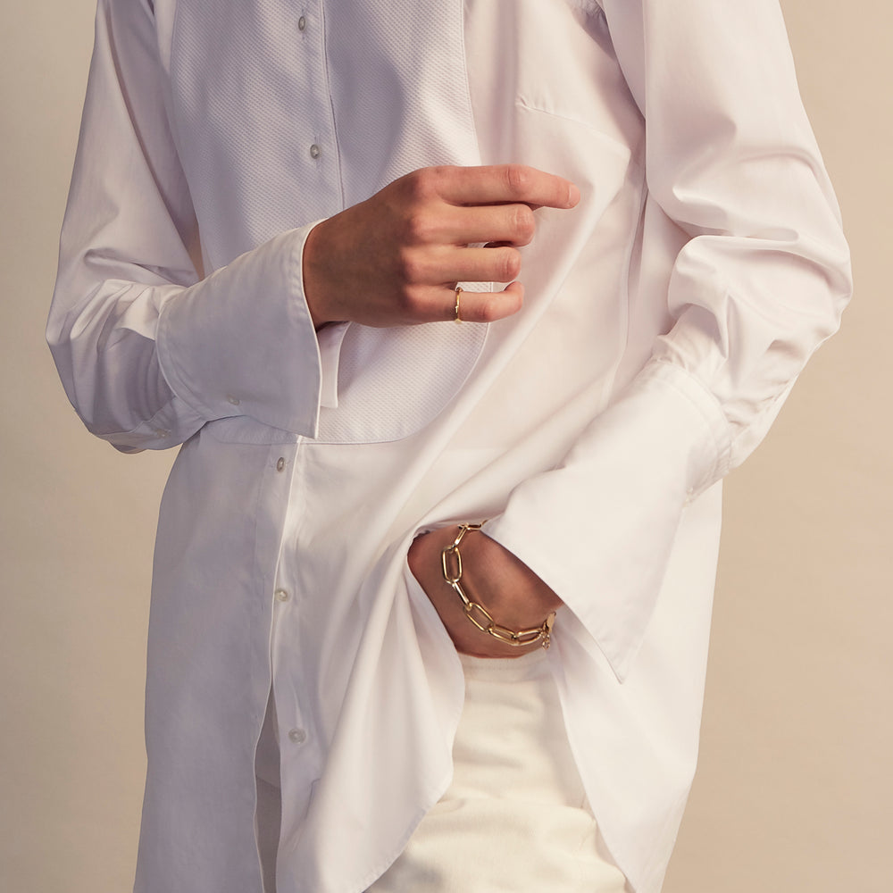 A person with curly hair wears the Turnbull and The Deck White Cotton Minimalist Shirt by Turnbull & Asser, paired with pants. Posed against a plain background, their minimalist silhouette is highlighted in this black and white image.