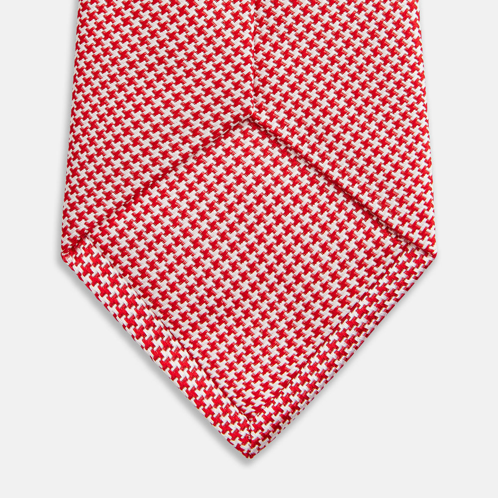 The HOUNDSTOOTH WHITE TULIP RED TIE by Turnbull & Asser features a refined red and white houndstooth pattern—an elegant accessory that elevates any crisp shirt or formal look.
