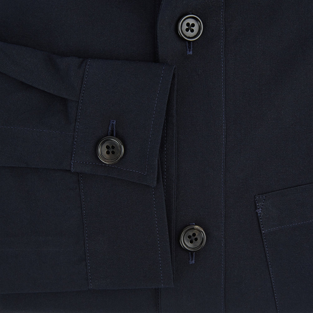 The Midnight Blue Hyde Overshirt by Turnbull & Asser is a plain, long-sleeve shirt in dark navy sanforised cotton with a single chest pocket, spread collar, and black buttons, shown laid flat on a white background.