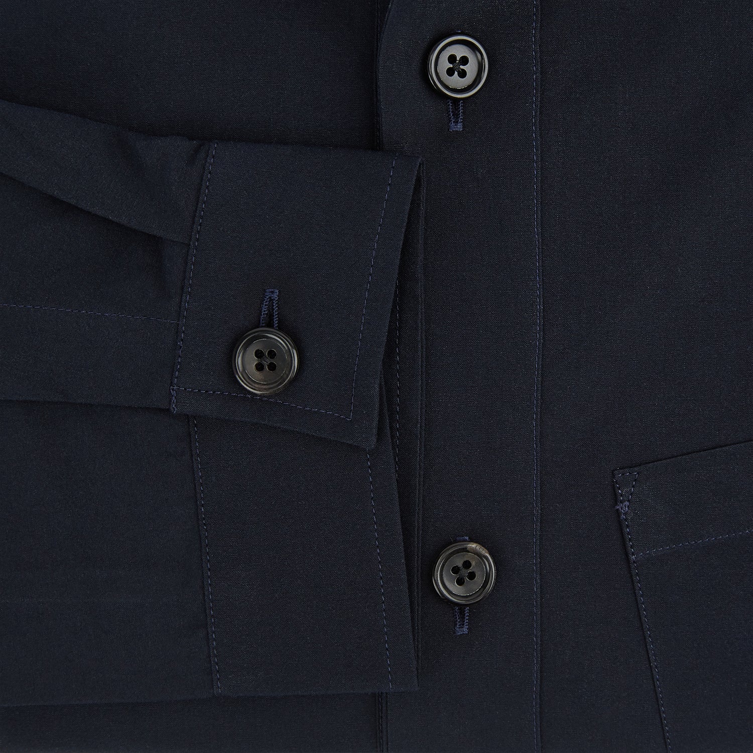 View 4 of product The Midnight Blue Hyde Overshirt by Turnbull & Asser is a plain, long-sleeve shirt in dark navy sanforised cotton with a single chest pocket, spread collar, and black buttons, shown laid flat on a white background.