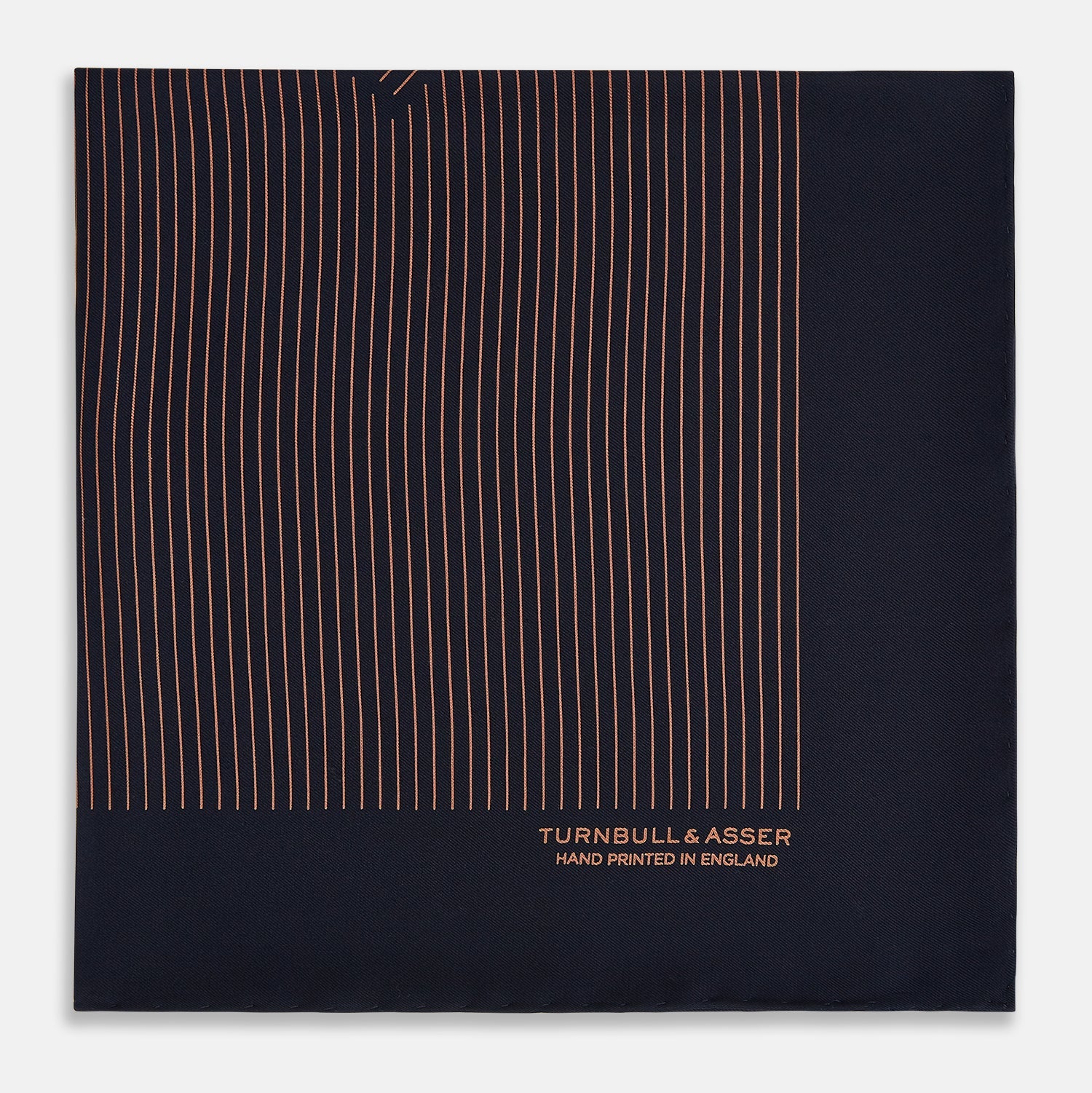 View 4 of product The Turnbull & Asser Navy and Blush Stripe Silk Pocket Square features thin blush stripes on navy silk, finished with "TURNBULL & ASSER HAND PRINTED IN ENGLAND" in the corner, highlighting its refined English craftsmanship.