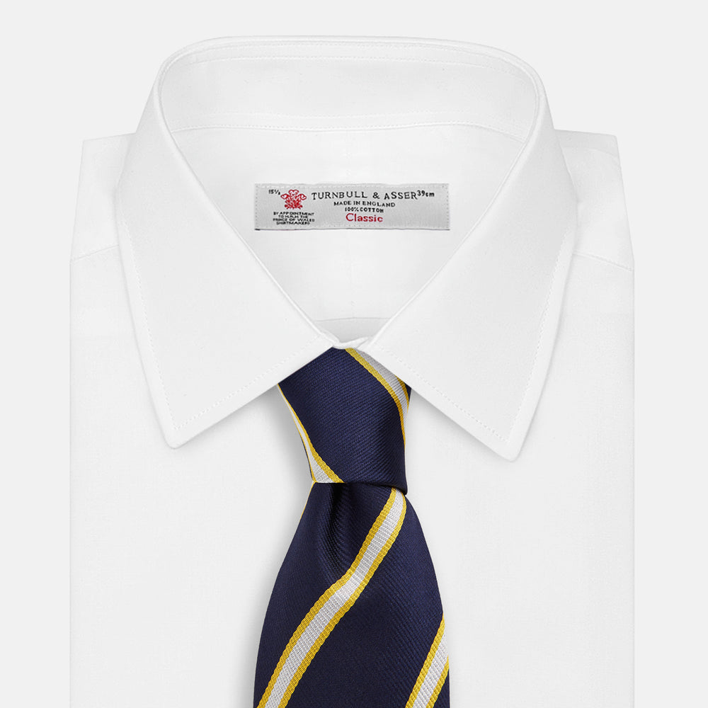 The Yellow and White Blazer Silk Tie by Turnbull & Asser, featuring diagonal white and yellow stripes on navy blue, is shown rolled up against a light gray background.