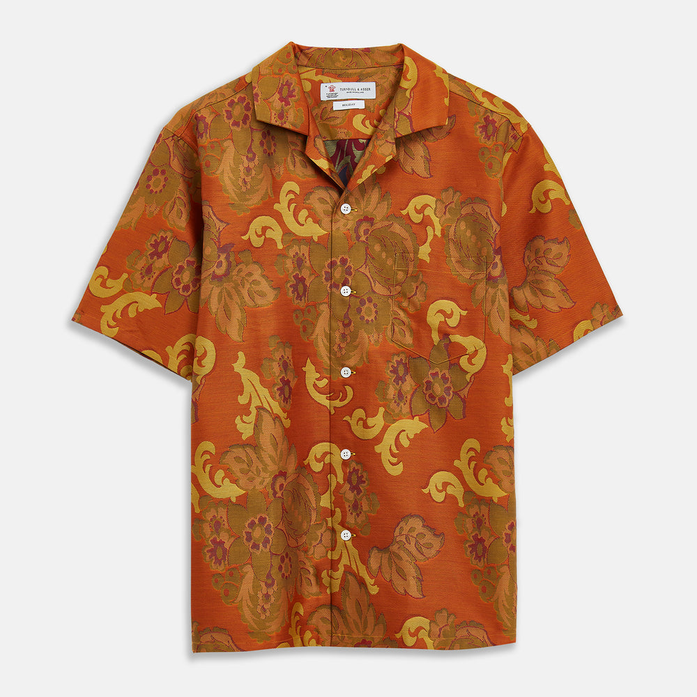 The Orange & Ochre Tapestry Weave Cotton Holiday Fit Shirt by Turnbull & Asser is a short-sleeve, revere collar shirt featuring a yellow and brown floral and leaf pattern on an orange base, finished with white buttons.