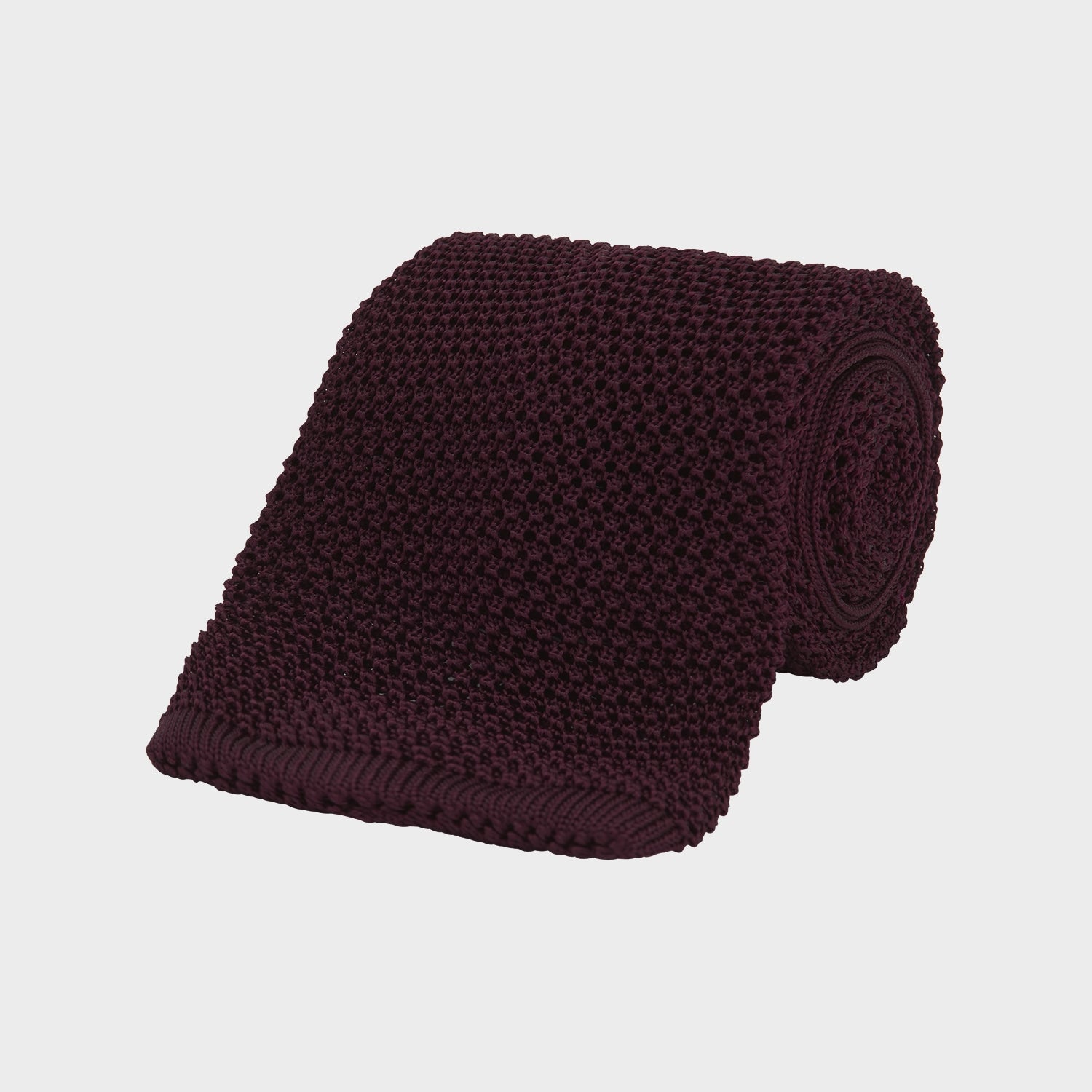 View 1 of product The Turnbull & Asser MTIE011-ZAI003 TIES 7.5CM is a plain burgundy tie shown rolled on a white background, featuring straight edges and textured knit—ideal for the modern gentleman’s versatile wardrobe.