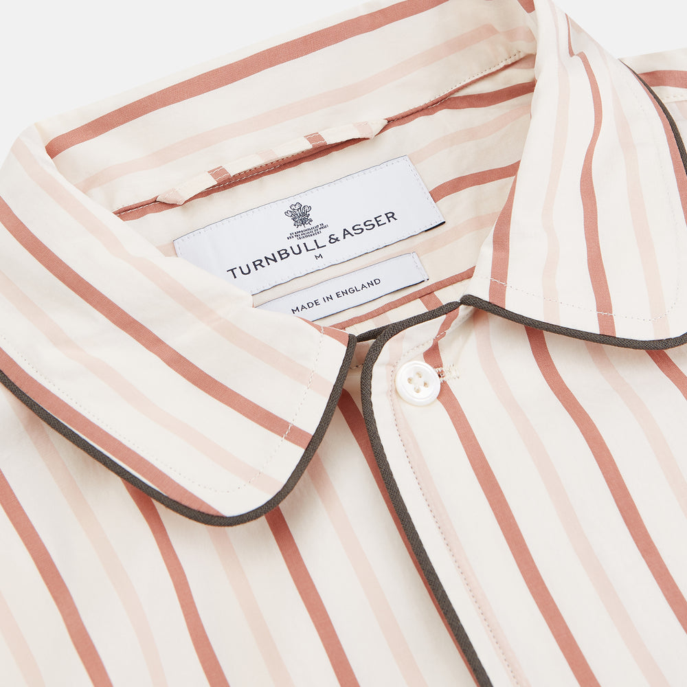 The Burgundy Multi Striped Cotton Sussex Nightshirt by Turnbull & Asser features long sleeves, knee length, a pointed collar, chest pocket, burgundy and beige stripes on white, buttoned cuffs, and a curved hem for classic sleepwear style.
