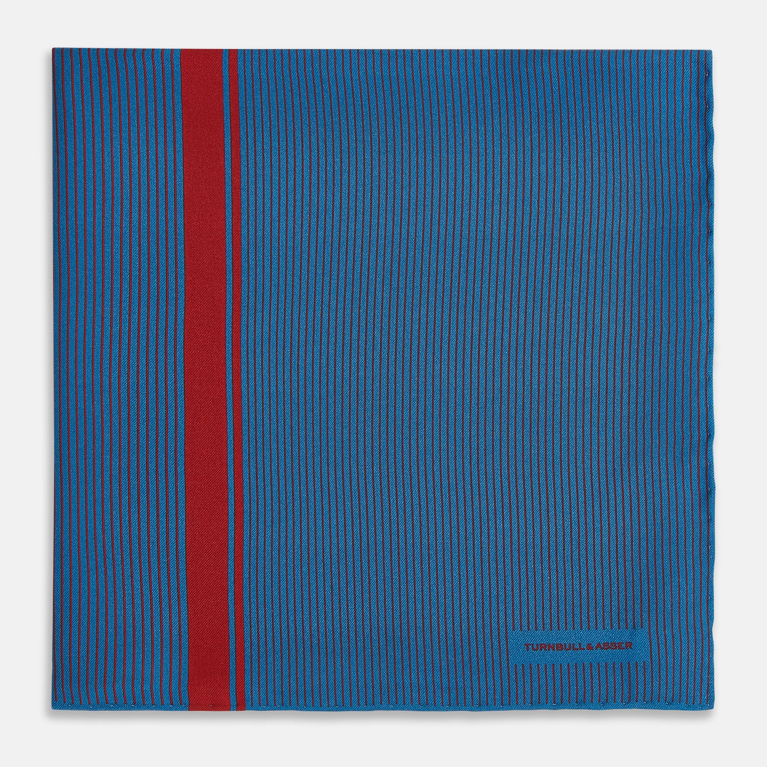View 3 of product A blue silk pocket square by Turnbull & Asser, featuring thin black stripes, a striking vertical red stripe, and a turned-over corner that reveals the reverse side. The brand name is printed discreetly in one corner.