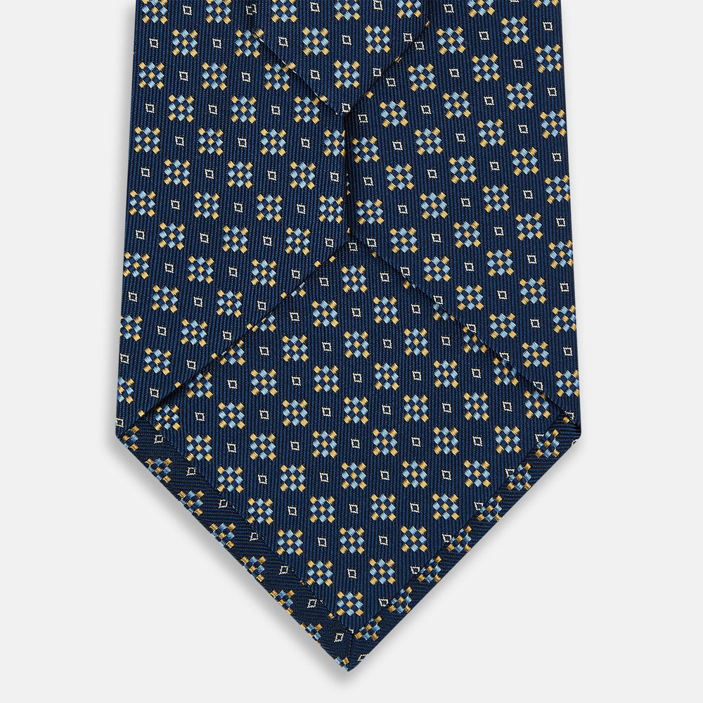 The Navy Diamond Silk Tie by Turnbull & Asser features a British-inspired geometric diamond pattern with small yellow and white squares against a navy silk background.