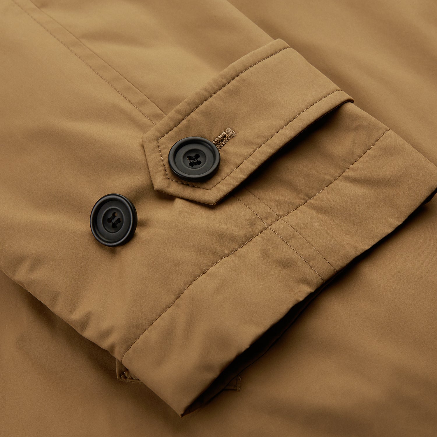 View 7 of product A person wears the Turnbull & Asser Camel Quintern Sealup Raincoat with Detachable Liner, paired with dark pants, standing against a plain light gray background, showing the sleek technical rainwear style with one hand in a pocket.