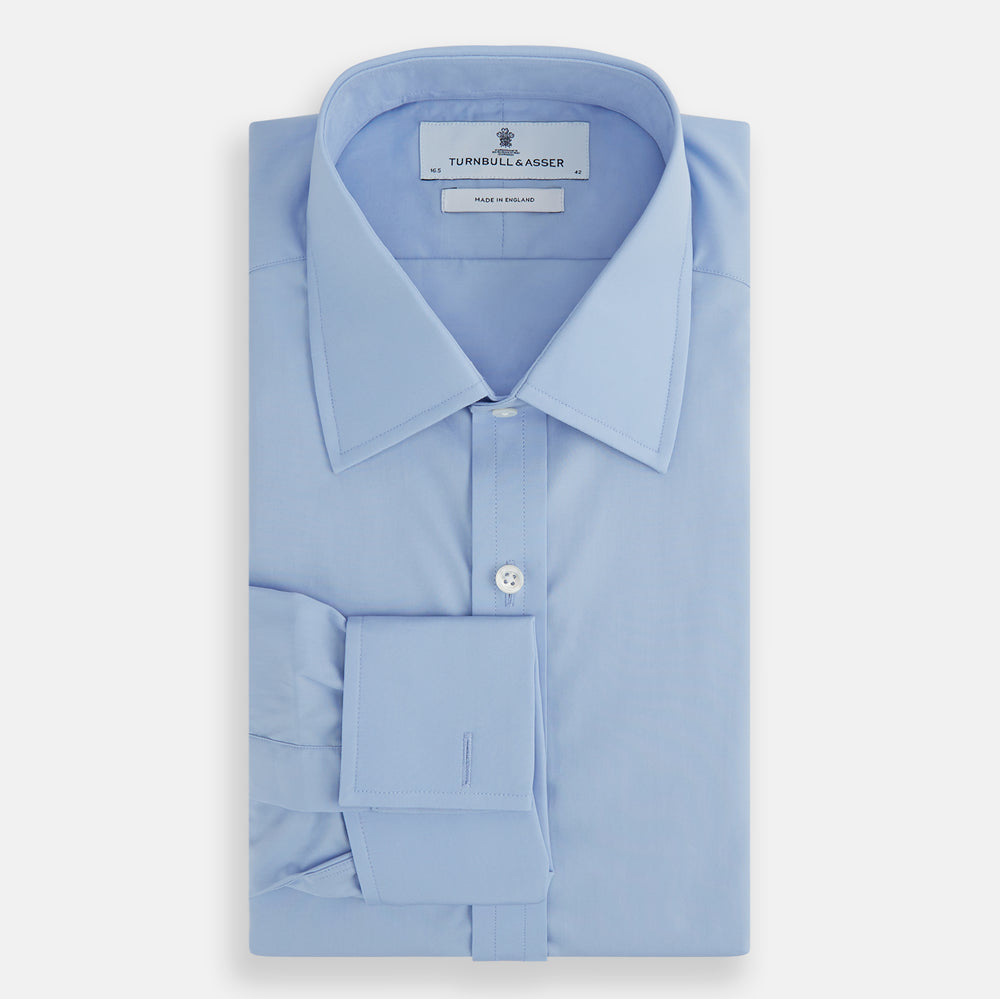 The Turnbull & Asser Blue Cotton Shirt features a T&A collar, double cuffs, and white buttons. This classic formal shirt is perfect for any gentleman and pairs effortlessly with a navy suit. Displayed on a plain white background.