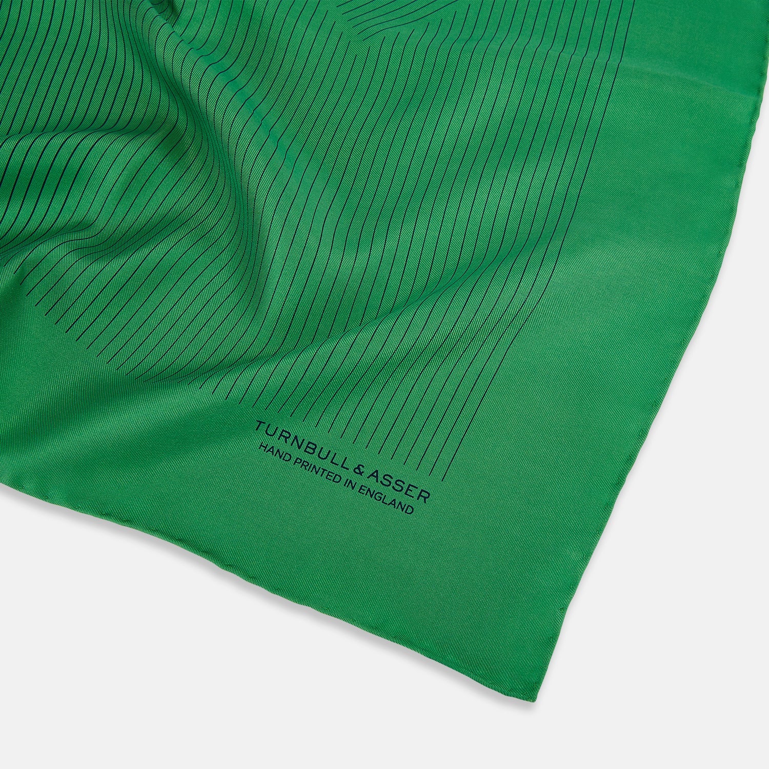 View 2 of product The Hunter Green Stripe Silk Pocket Square by Turnbull & Asser features thin black vertical stripes on one corner and “Turnbull & Asser Hand Printed in England” printed in black, reflecting classic British heritage.